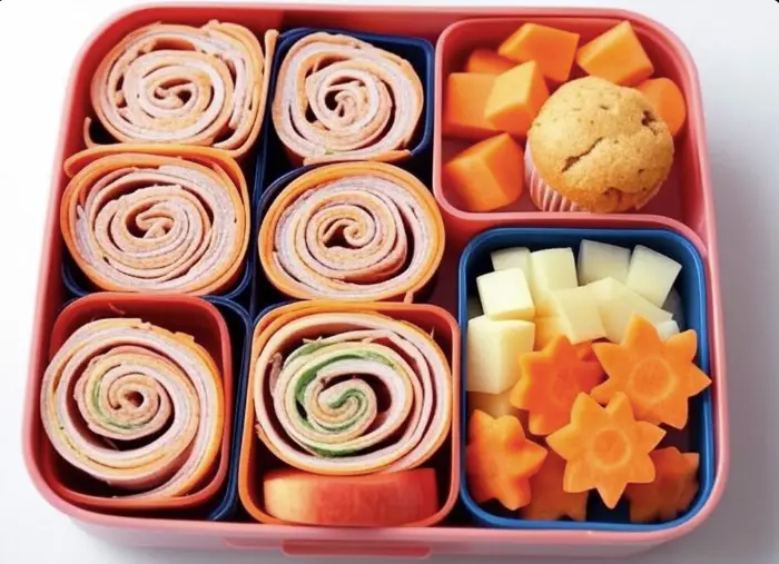 Creative kids' bento lunchbox with turkey pinwheels, fruit, and veggie shapes.